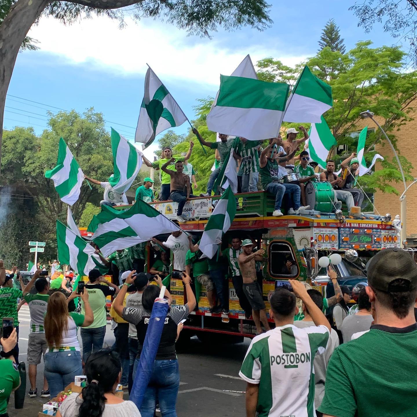 Atlético Nacional fans waving green and white flags from the roof of a painted chiva bus