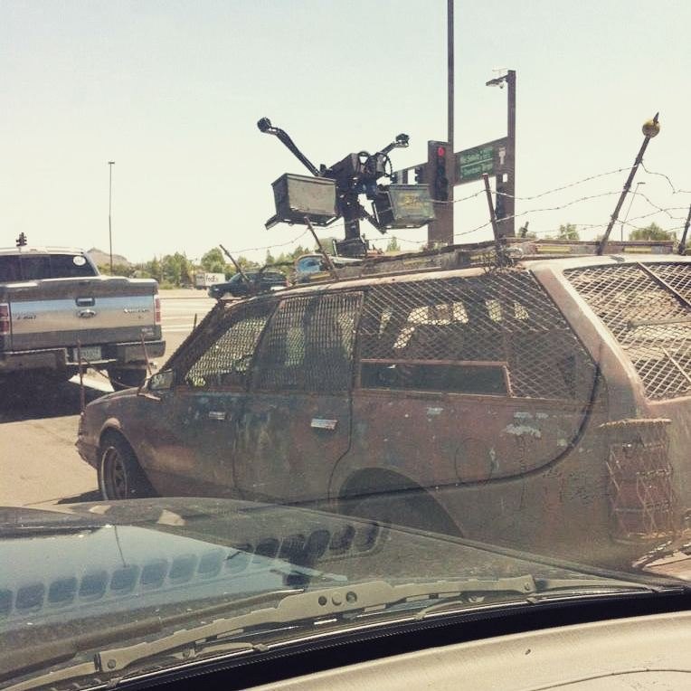 A rusted station wagon armored with mesh and a mock turret, stopped at a Phoenix intersection