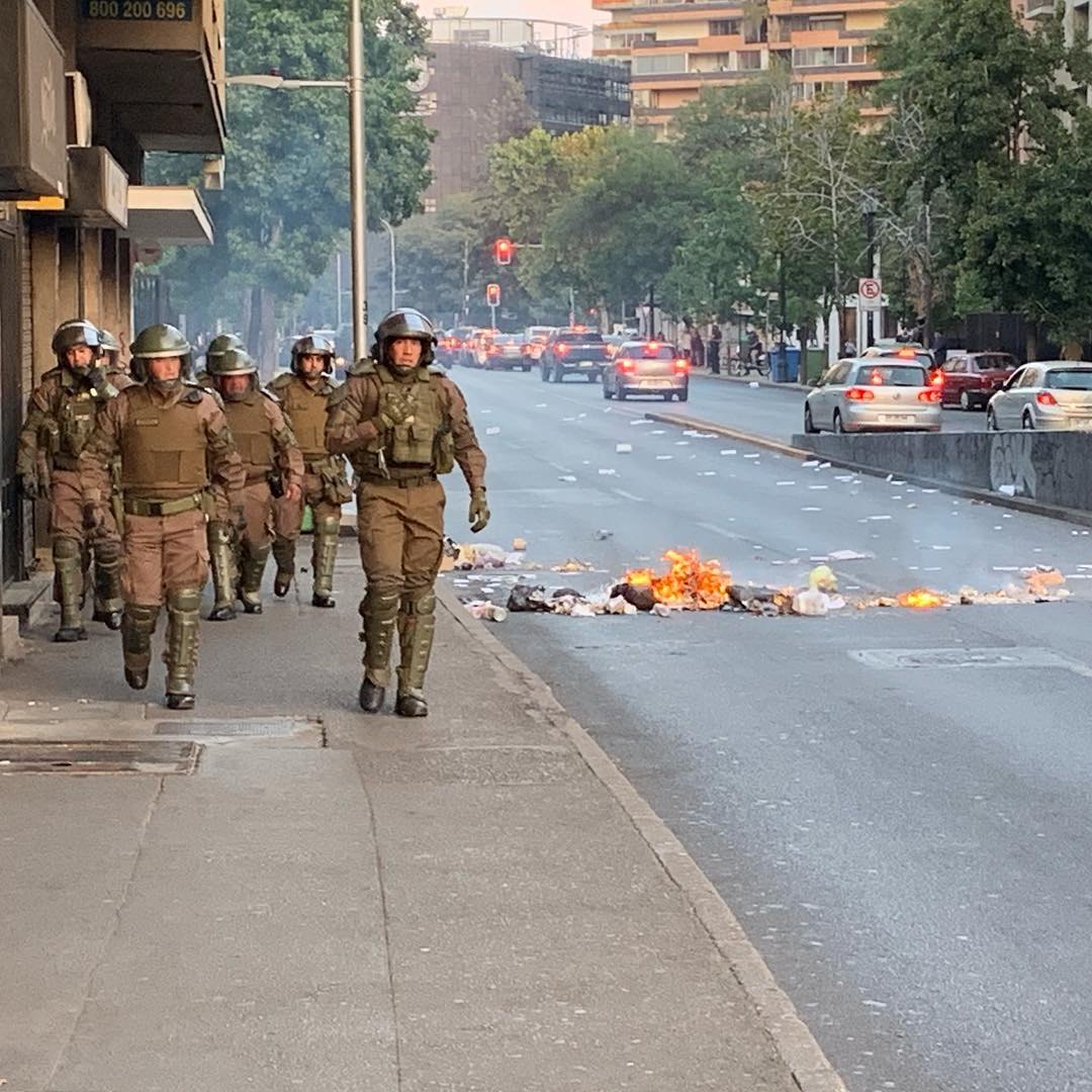 Carabineros in riot gear walk past a burning barricade on a Santiago street