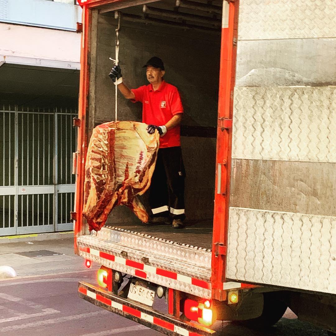A deliveryman in a red shirt unloads a side of beef from a truck on a Santiago street