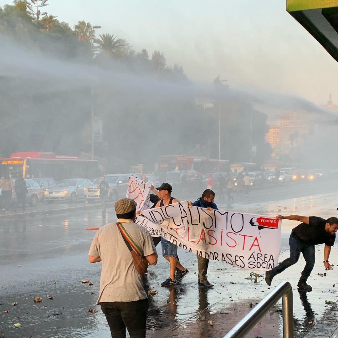A water cannon sprays protesters holding a union banner on a Santiago avenue